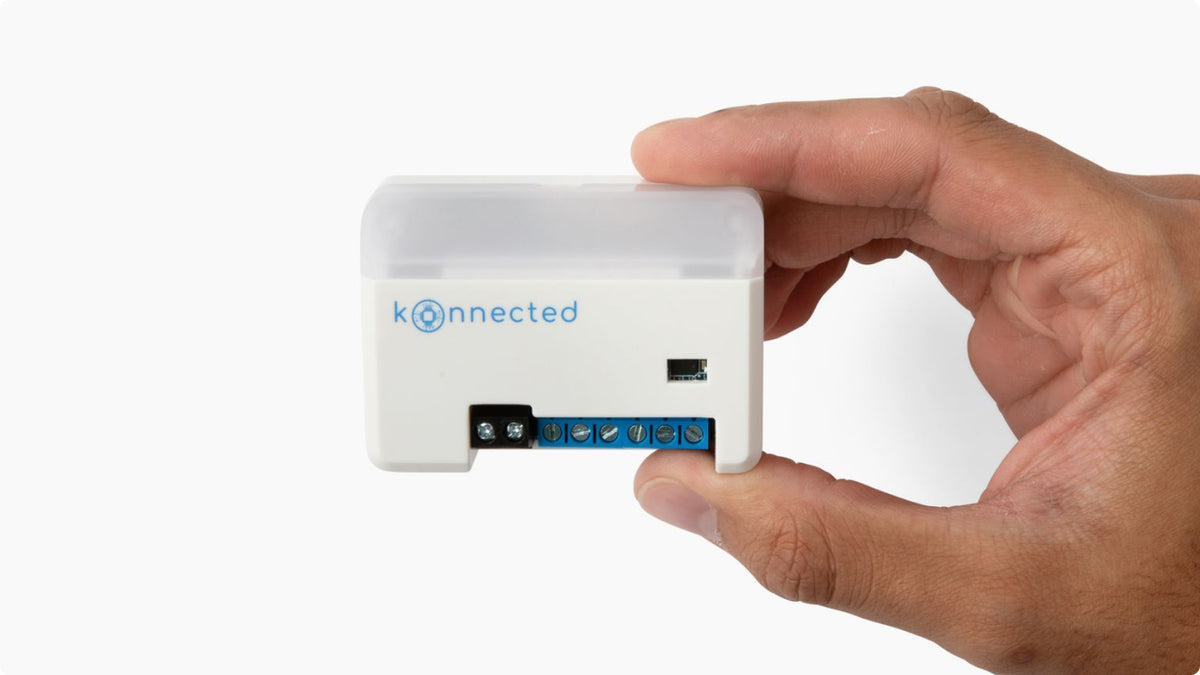 A Konnected garage door opener controller held between a thumb and forefinger